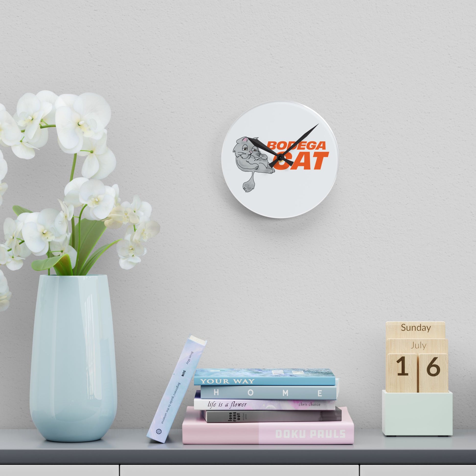 Decorative clock with 'Bodega Cat' design on a shelf with books and a vase.