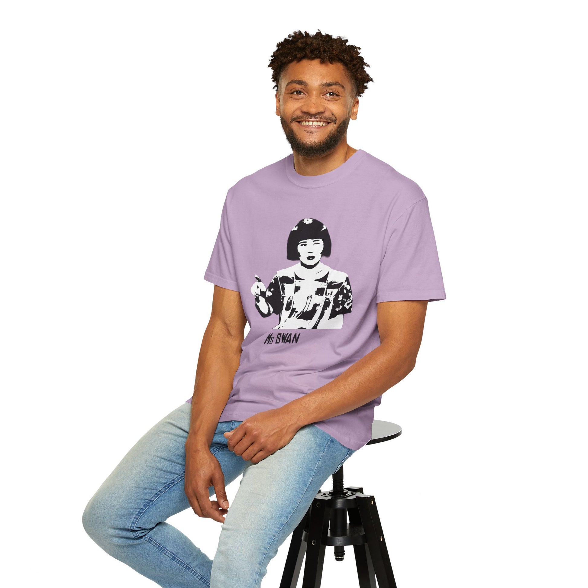 Man sitting on stool wearing lavender Ms. Swan T-shirt, smiling at the camera.