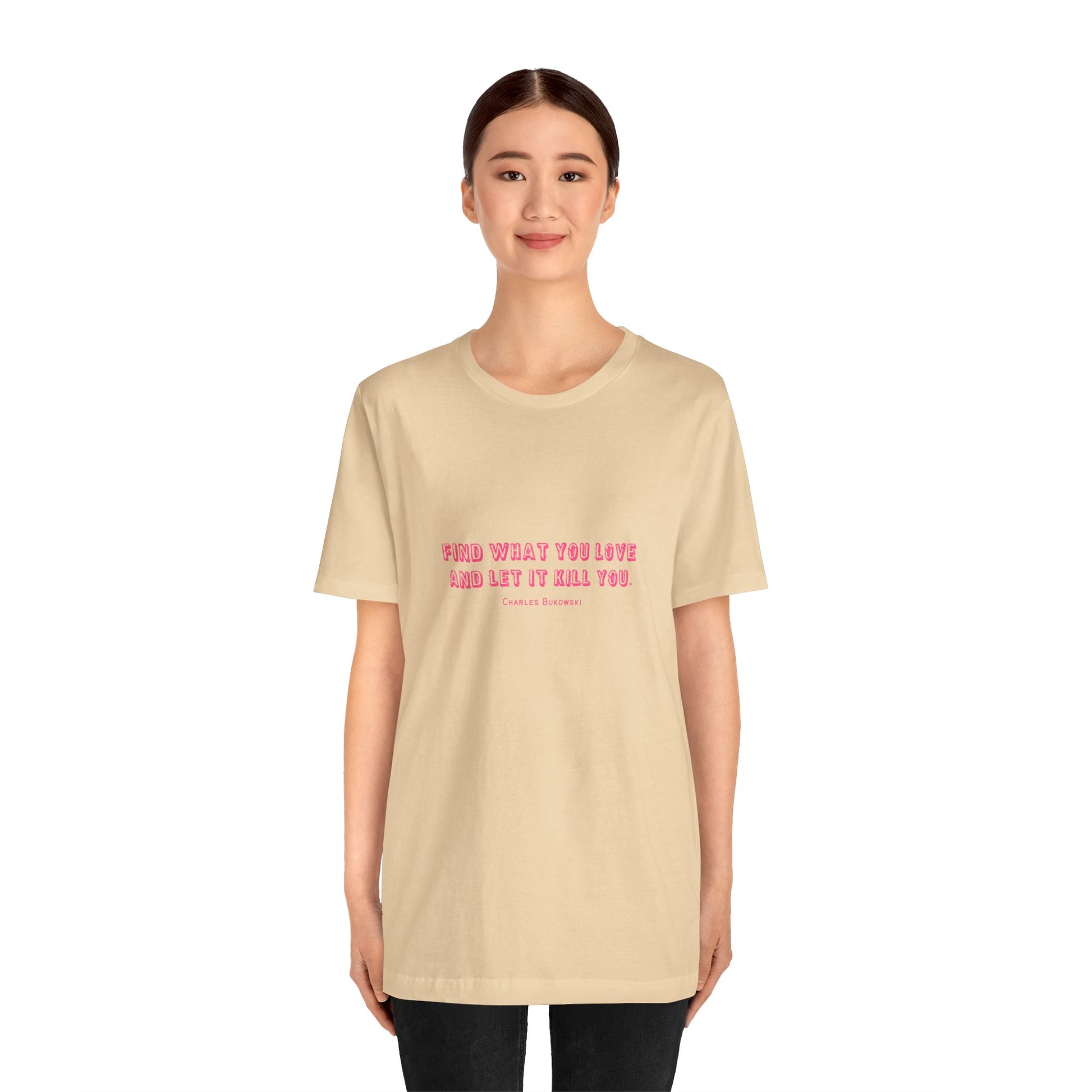 Woman wearing a sand colored Bukowski quote t-shirt with black pants.