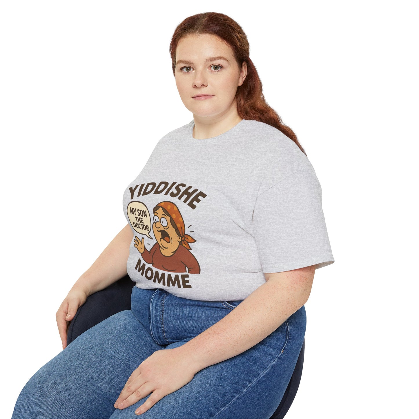 Plus-size model seated and smiling in a gray Yiddishe Momme T-shirt and jeans.