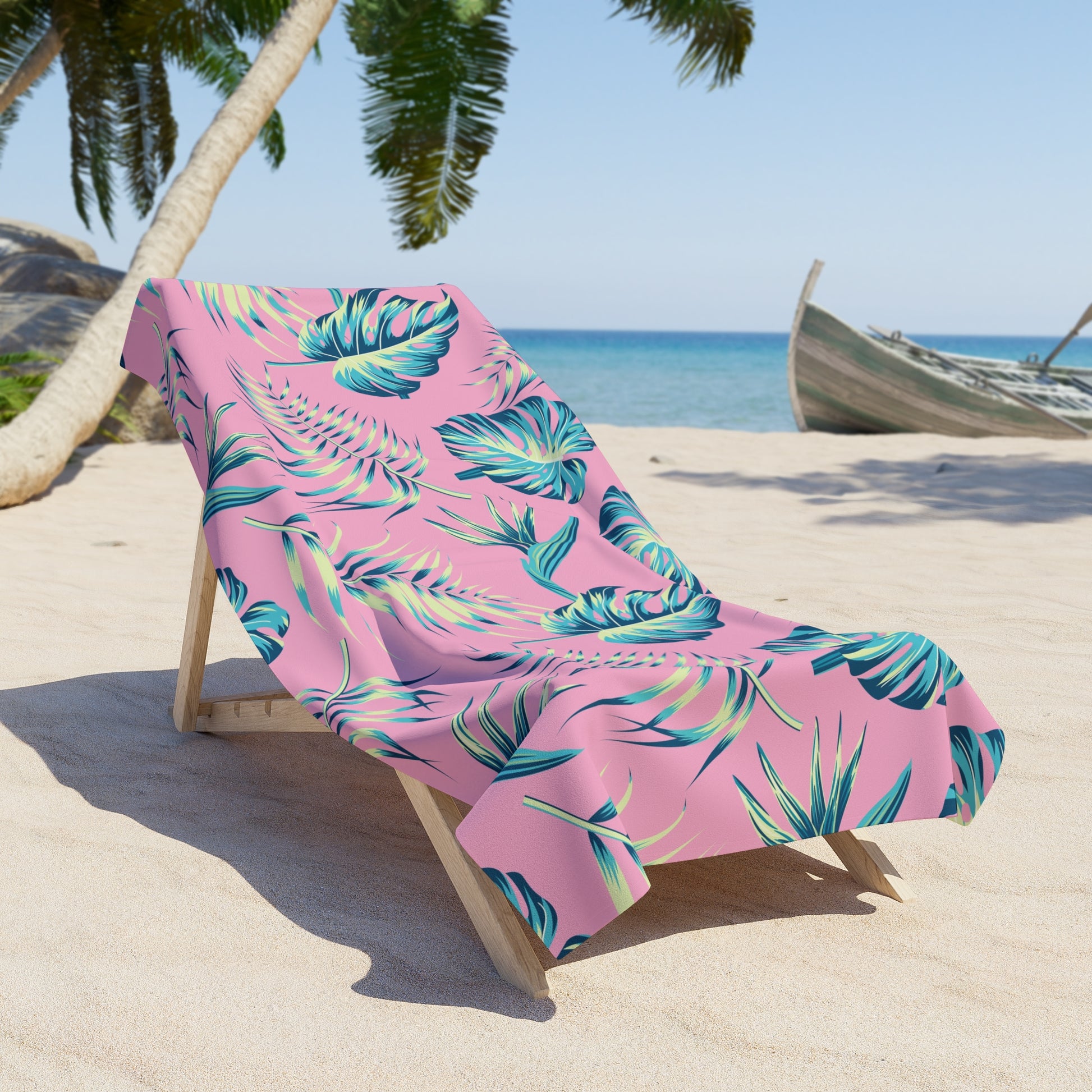 Tropical leaf patterned towel draped over a lounge chair on a sandy beach with palm trees and ocean in the background.