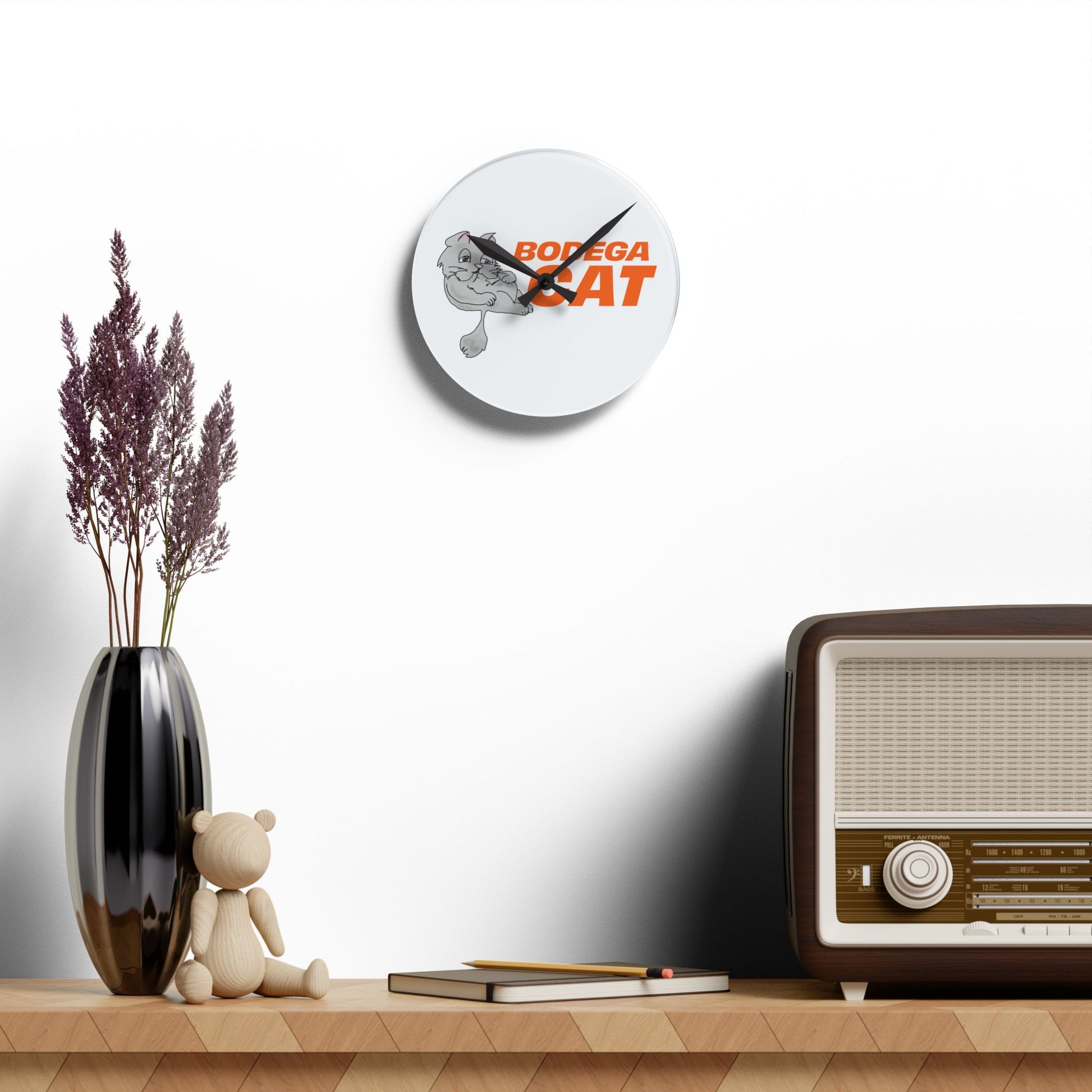Wall clock with 'BOGEGA CAT' design on a shelf with decorative items.