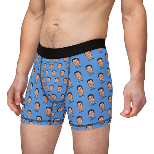 Front angled view of a man wearing Elon Musk Boxer Briefs featuring cartoon Elon faces on blue fabric.
