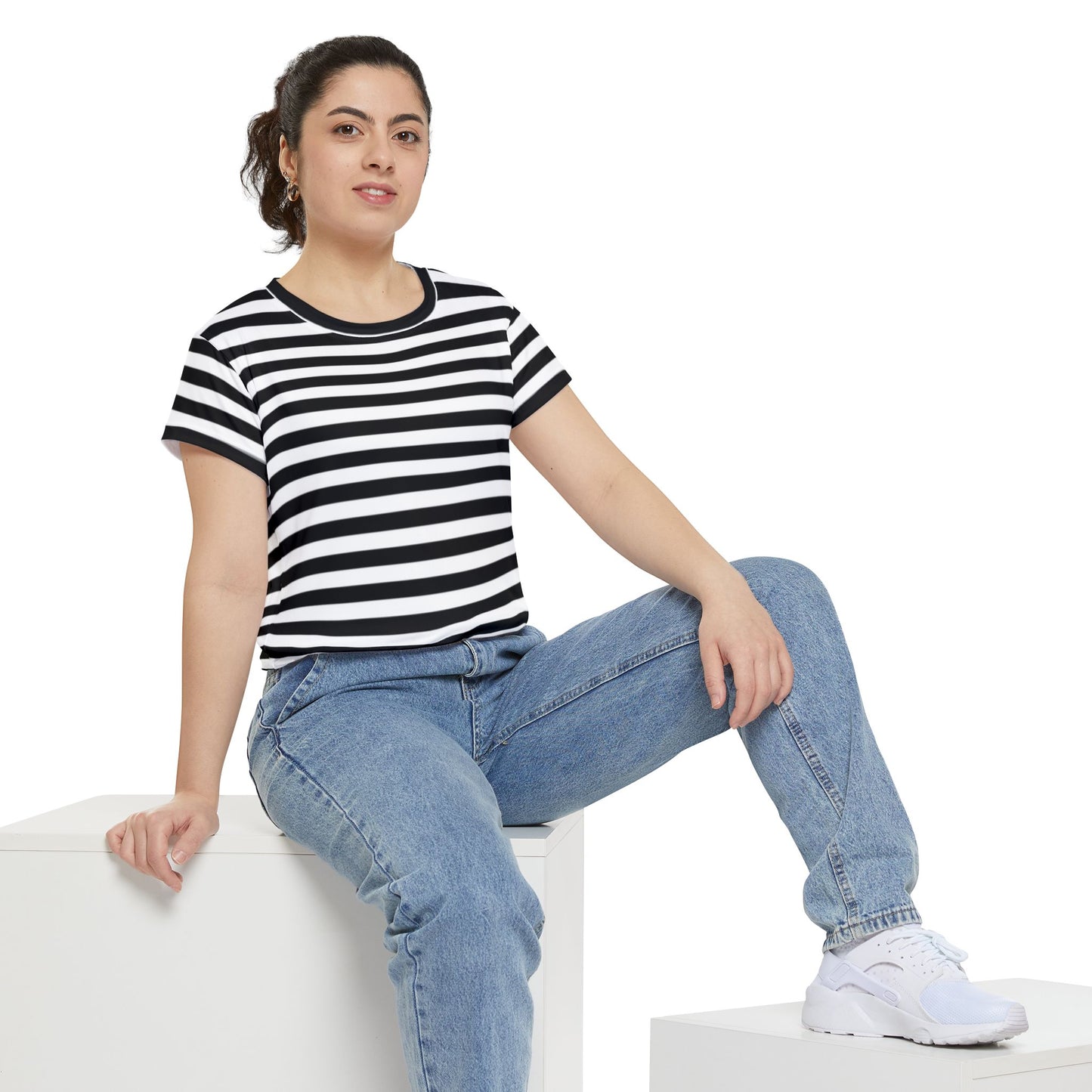 Woman wearing a black and white striped tee with jeans, sitting casually on a white block.