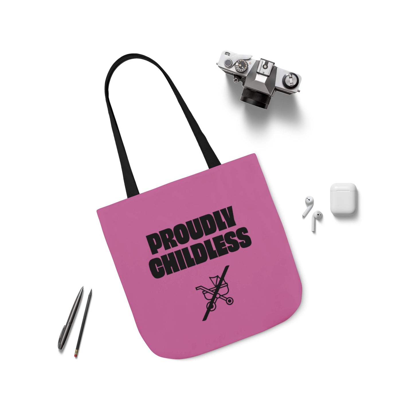 Flat lay of pink Proudly Childless tote bag with black strap and accessories