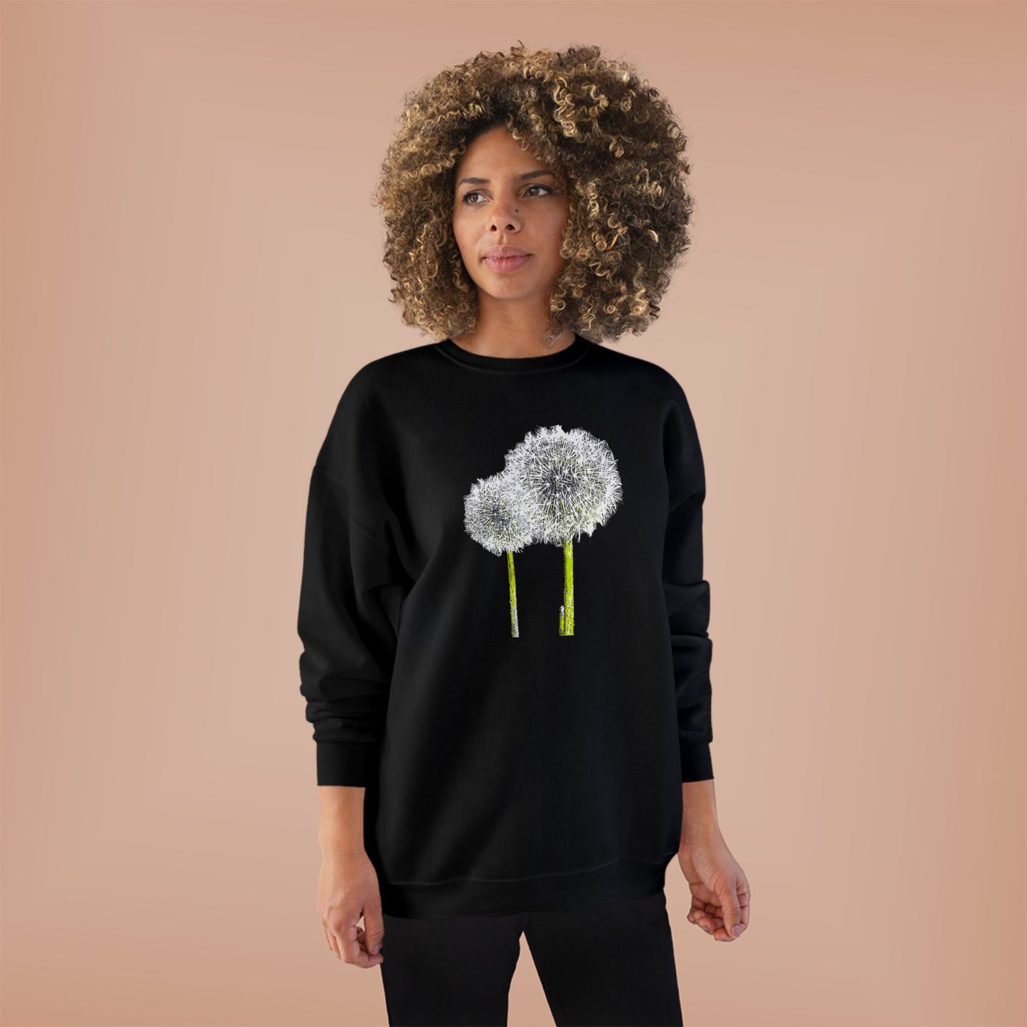 Woman in black Tantrum Media Dandelion Unisex Sweatshirt with white dandelion print, peach background