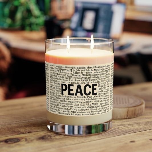 Candle in a glass container with 'PEACE' text on a wooden surface