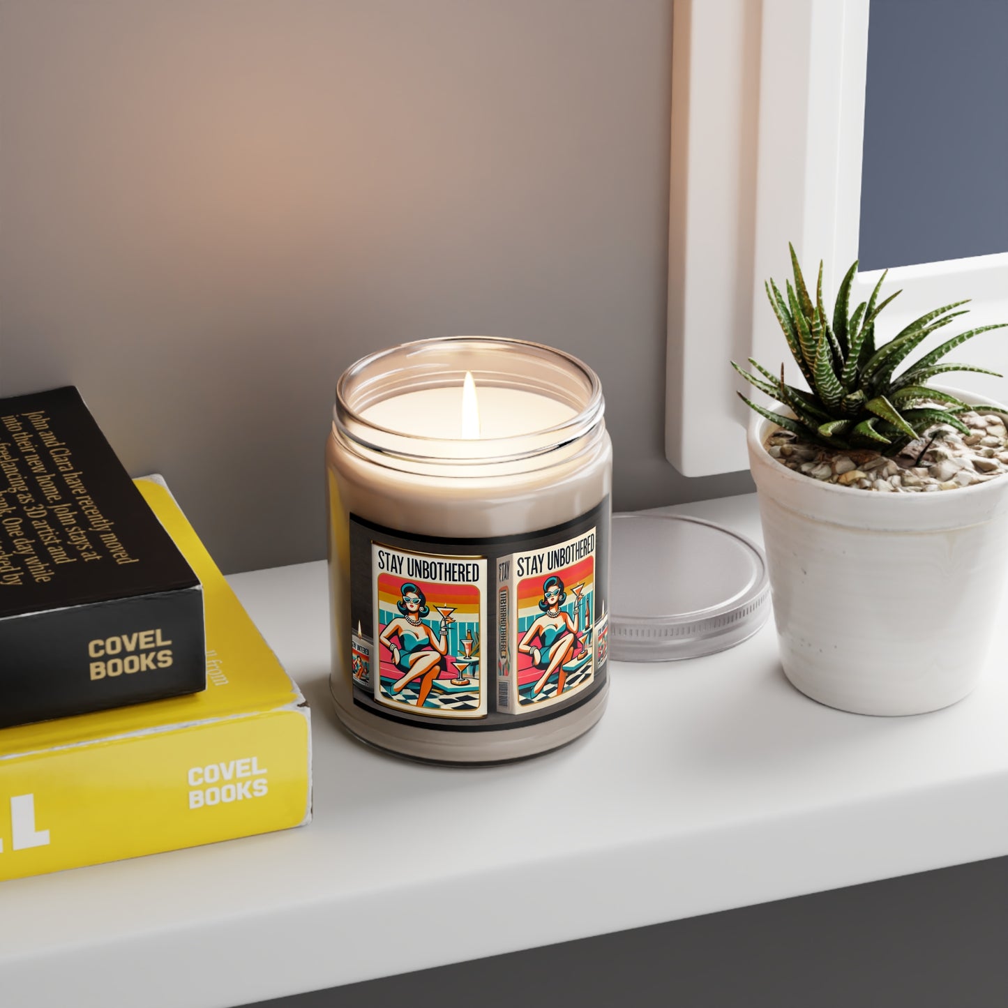 Stay Unbothered Candles Fresh Balsam lit on a shelf next to a plant and books in a calm home setting
