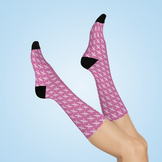 Pink Proudly Childless crew socks with black heel and toe shown on crossed legs against light blue background