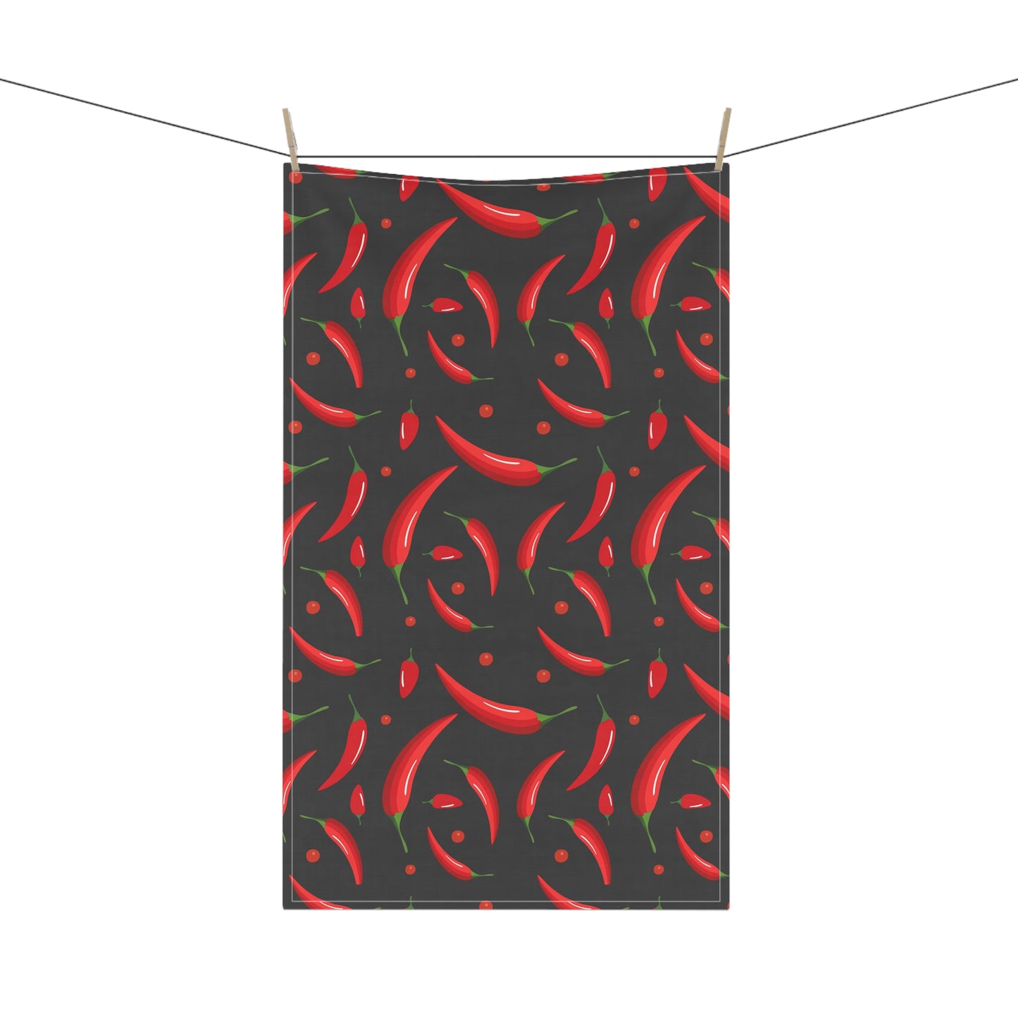 Tea towel with red chili pepper pattern on a black background, hanging on a line.