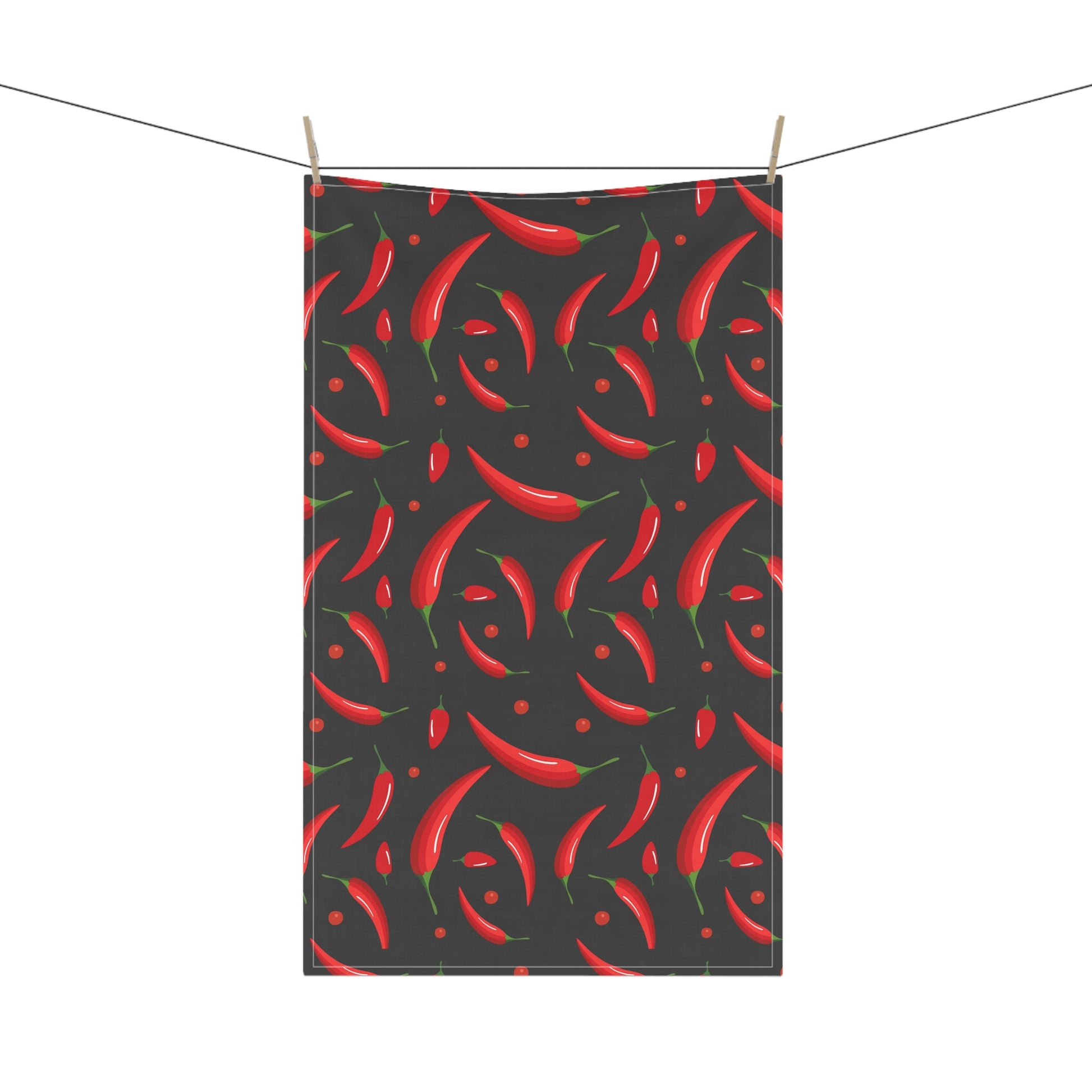 Tea towel with red chili pepper pattern on a black background, hanging on a line.