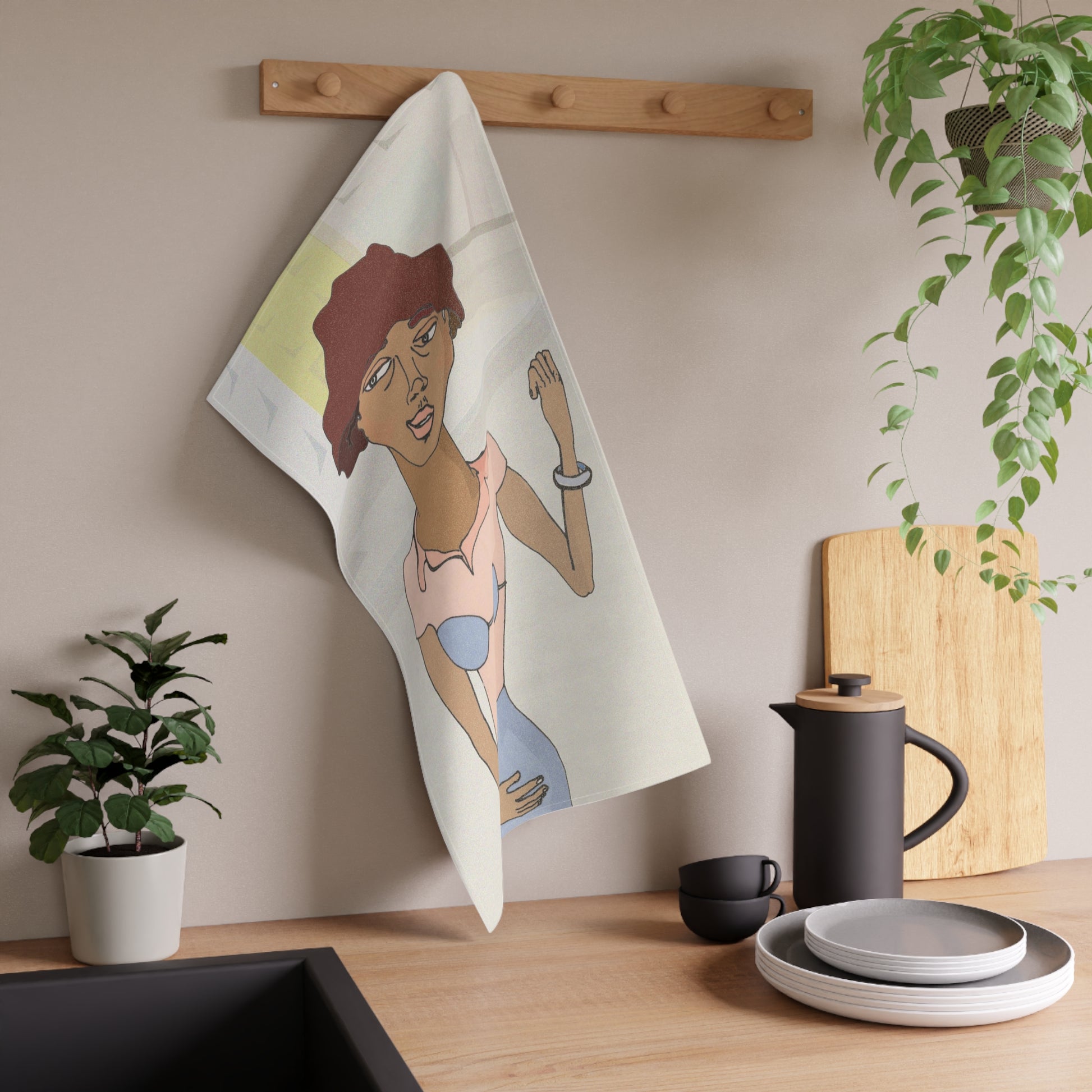 Morenita Kitchen Towel hanging on a wooden hook in a modern kitchen, styled with plants and coffee accessories.