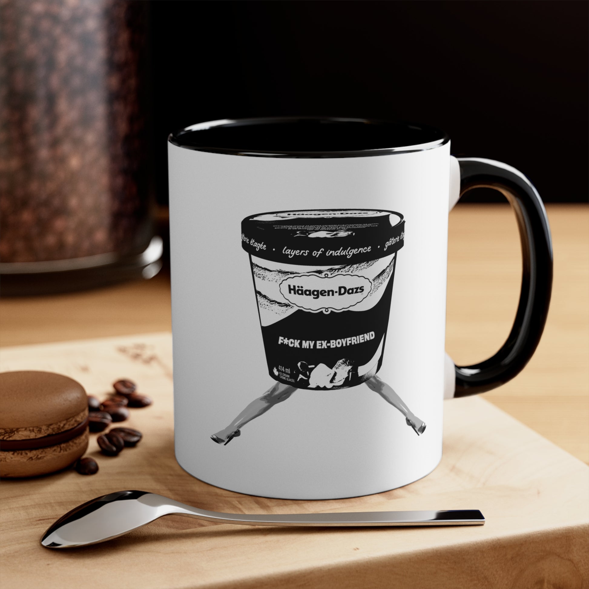 White mug with black handle on wooden table with spoon and coffee beans