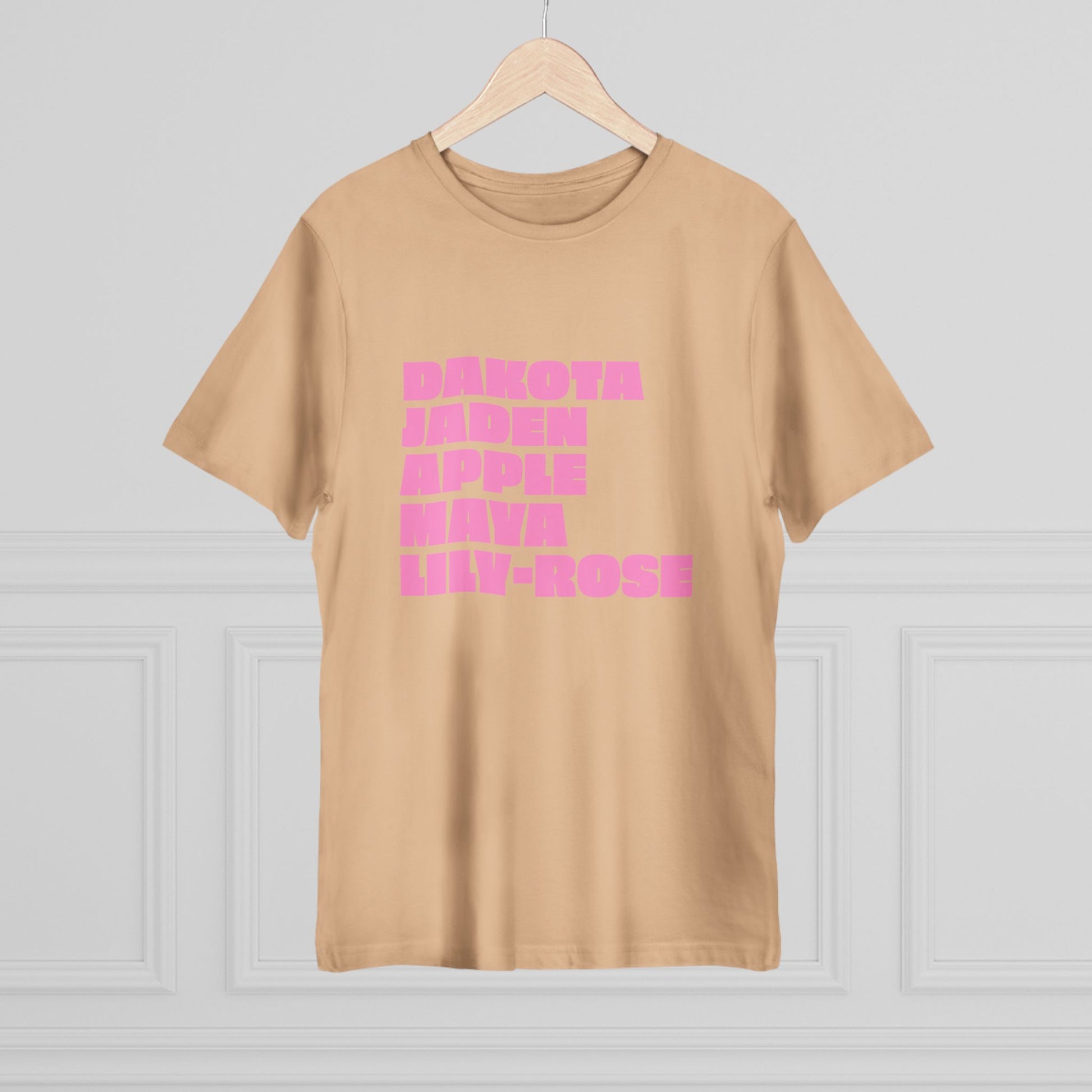 Beige t-shirt with pink text on a hanger against a white wall