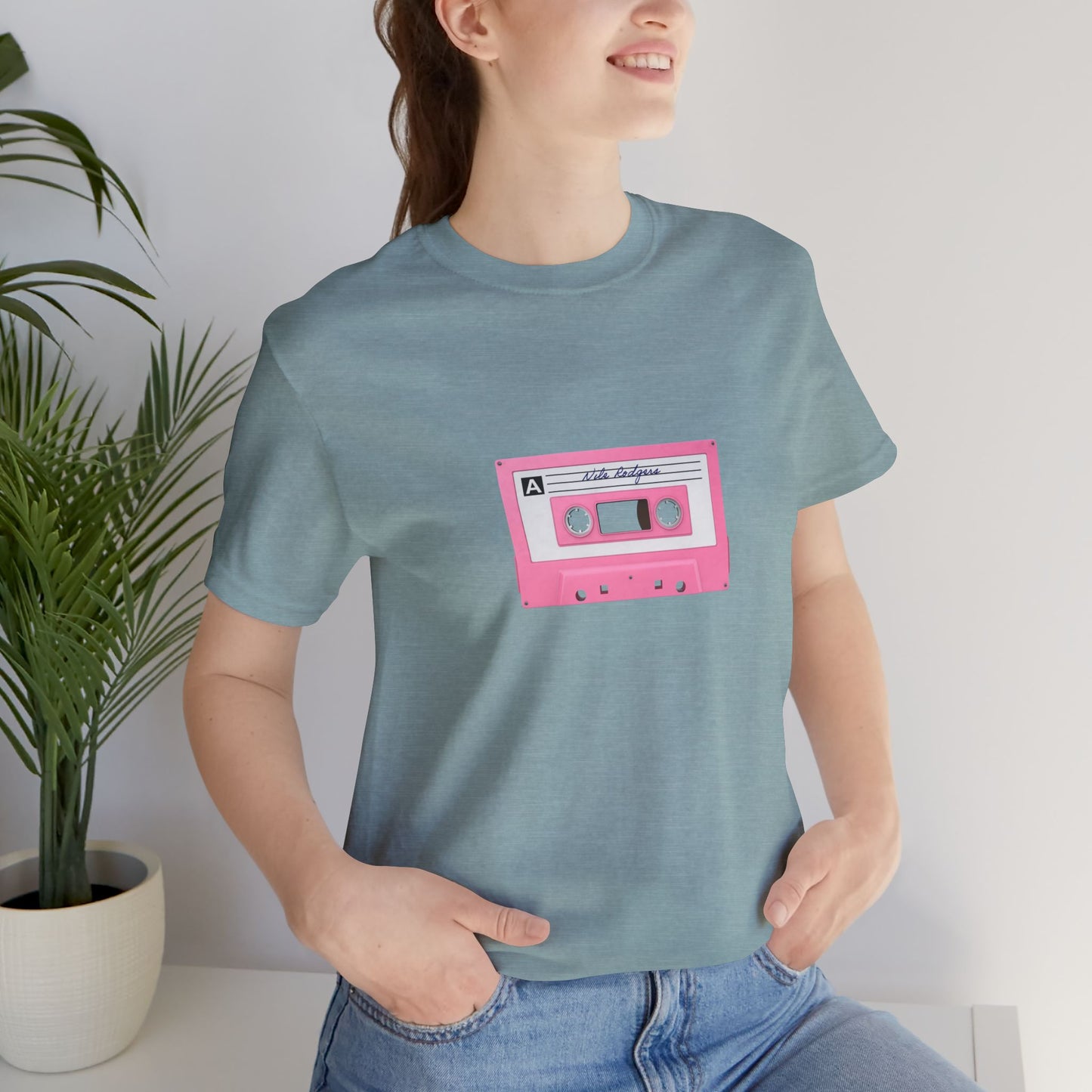 Person wearing a blue t-shirt with a pink cassette tape graphic