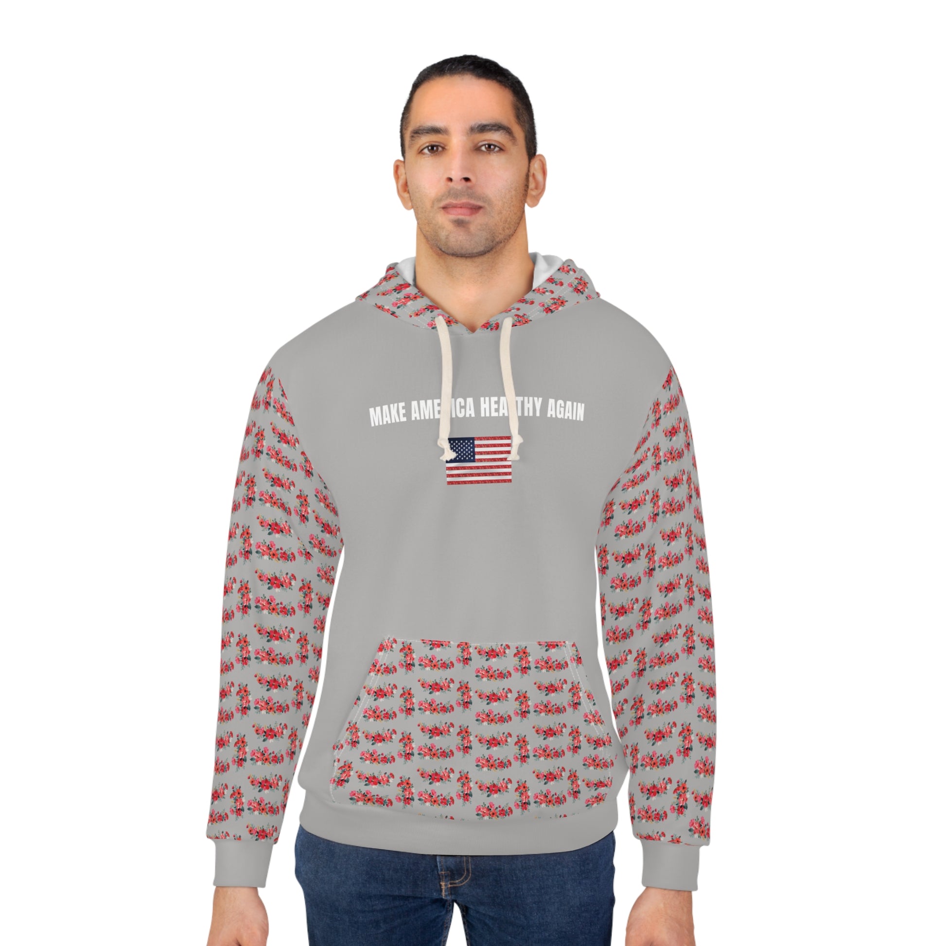 A person wearing a gray unisex hoodie that says "Make America Healthy Again" above an American flag graphic, featuring red floral patterned sleeves and front pocket, standing against a white background.