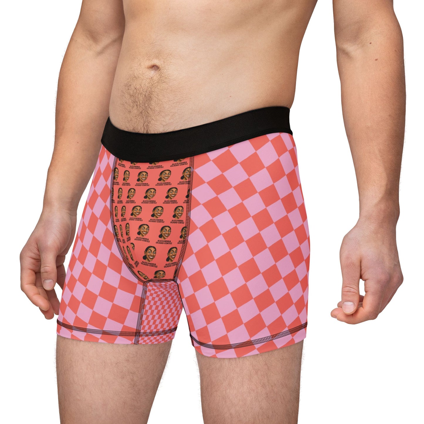 Man wearing pink and red checkered boxer briefs featuring repeated AOC face print on the front pouch panel.