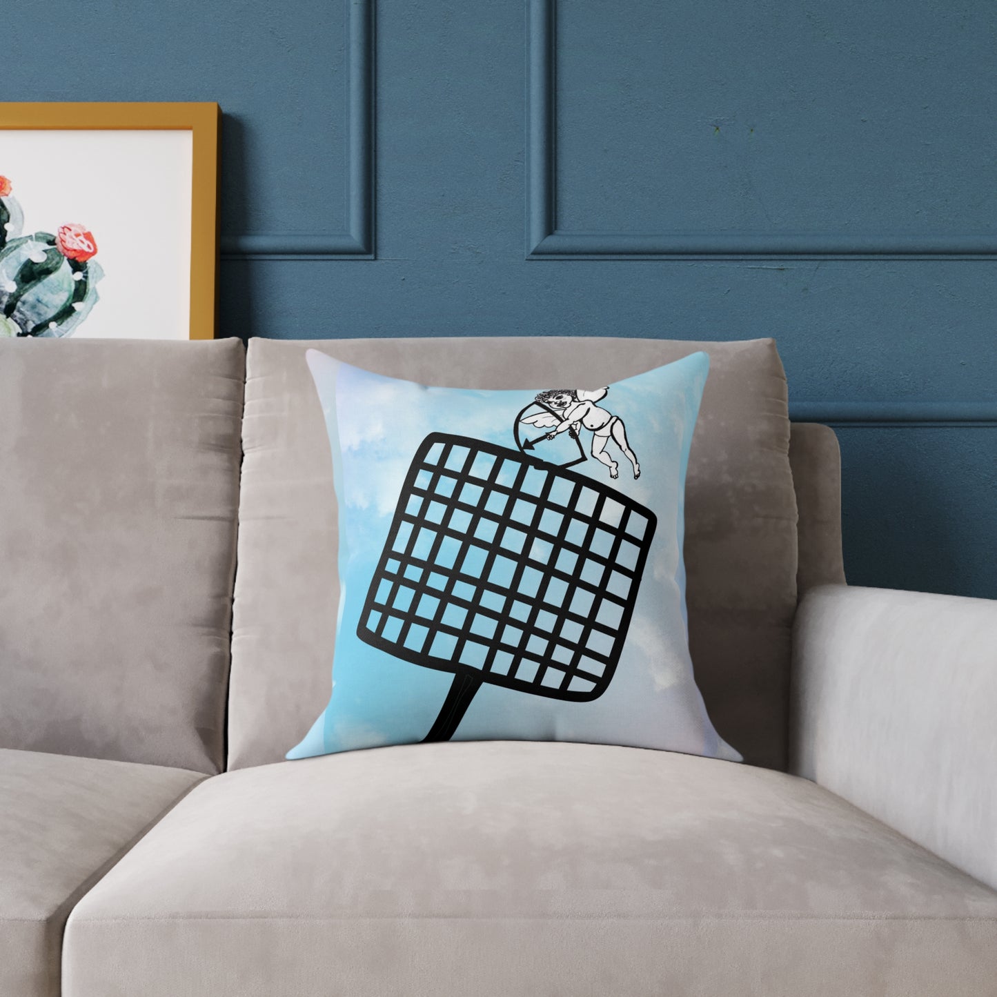 Blue and white throw pillow with a hand-drawn Cupid aiming an arrow while a large fly swatter looms in the foreground, placed on a modern couch.