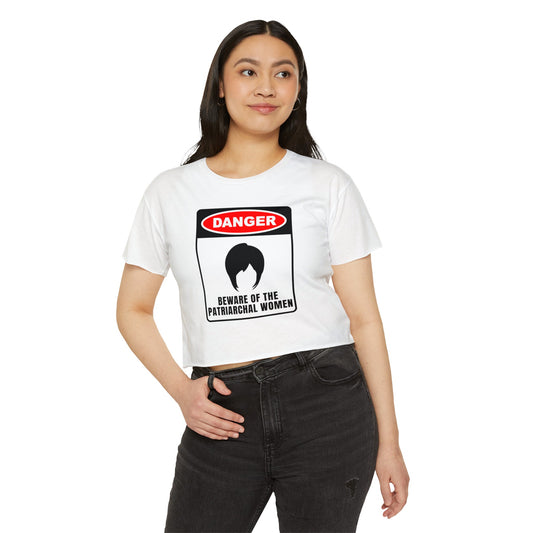 Woman wearing a white crop top with a bold “Danger: Beware of the Patriarchal Women” graphic featuring a silhouette of a woman's hairstyle.
