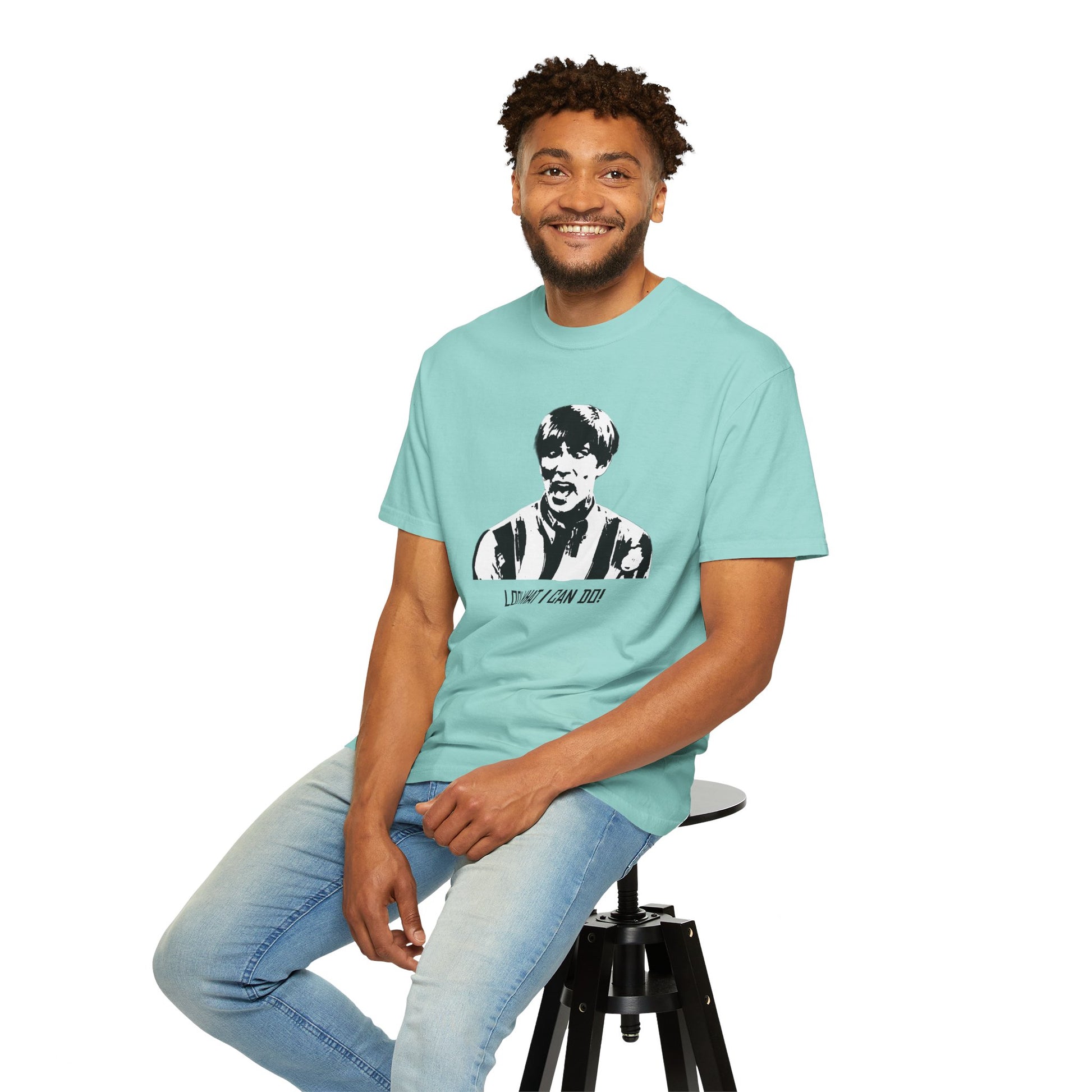 Man modeling mint green Stuart MadTV T-shirt while seated, hands on legs.