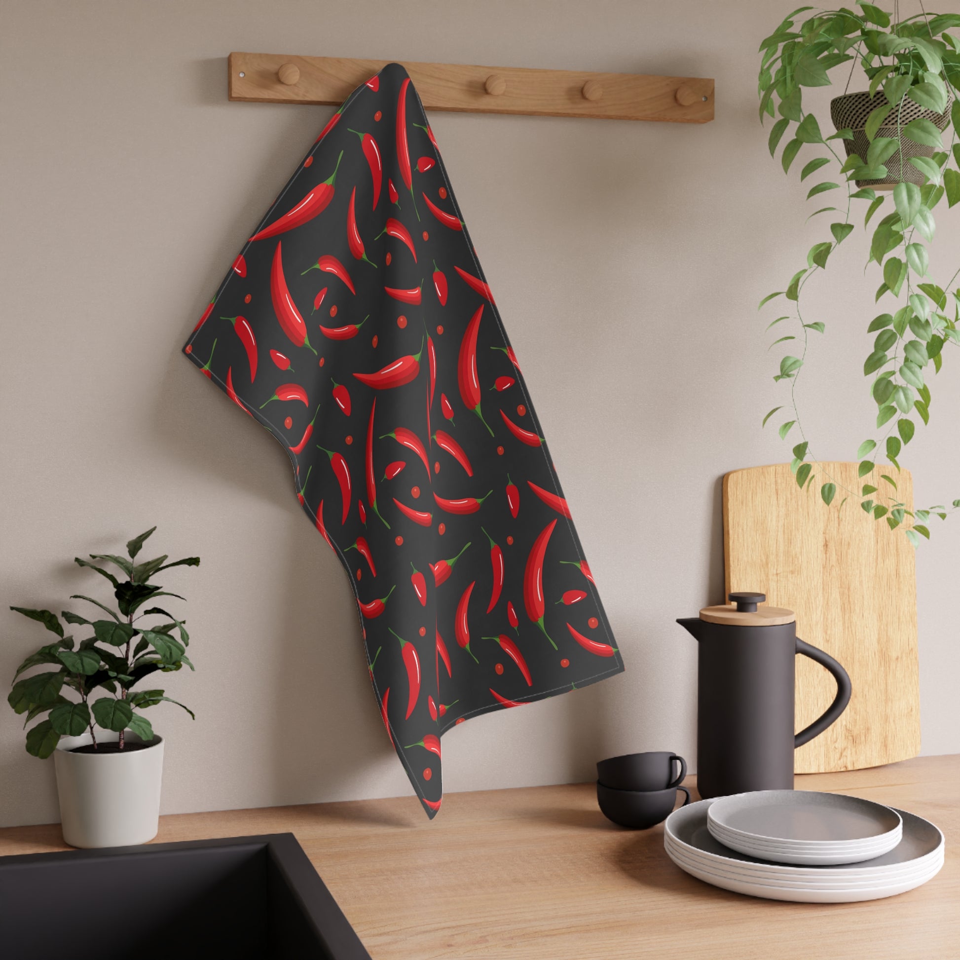 Black towel with red chili pepper pattern hanging on a wooden rack in a kitchen setting.