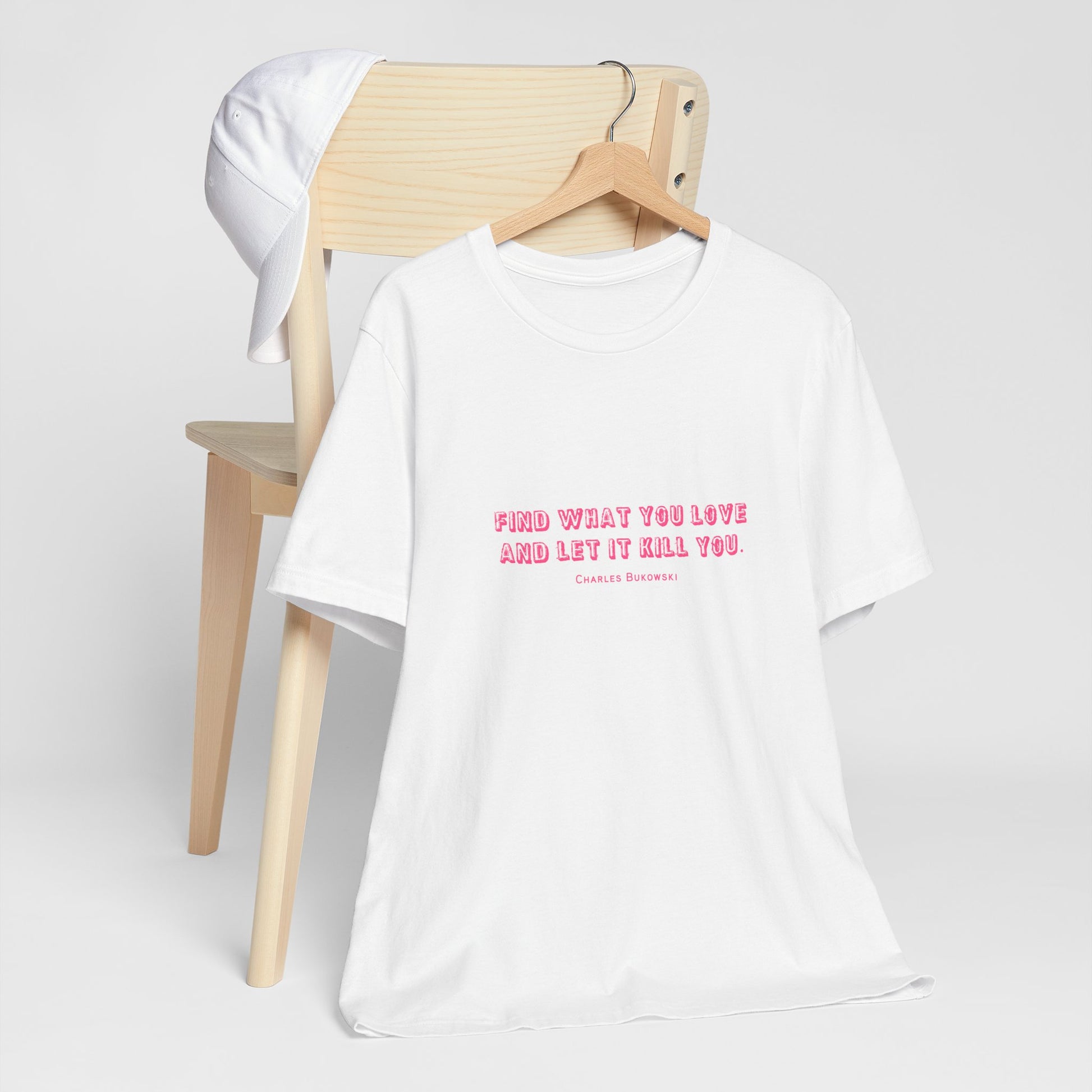 A white Bukowski quote t-shirt hanging from a hanger hooked to the back of a chair