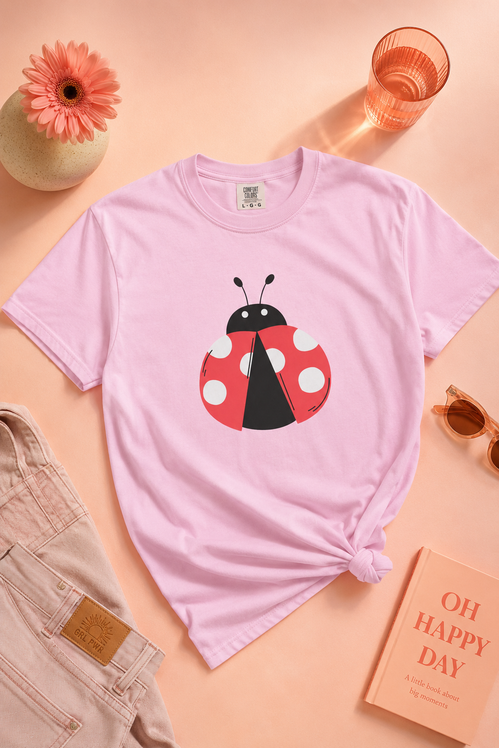 Flat lay of pink Ladybug Graphic Unisex T-Shirt with pastel accessories