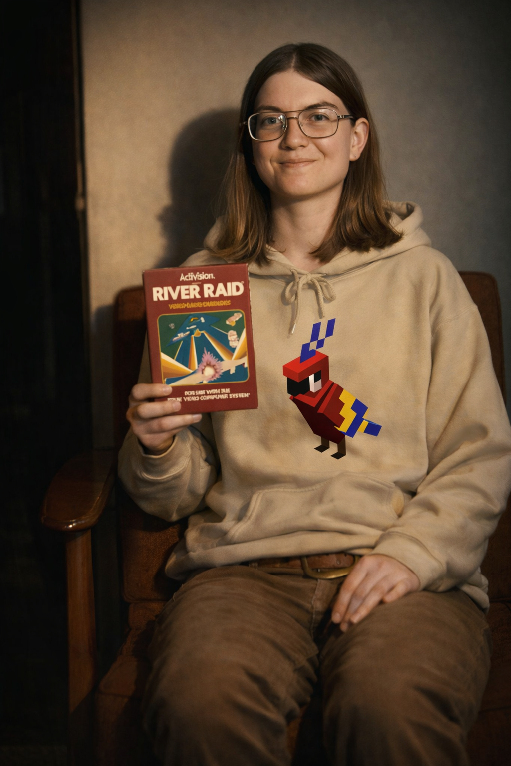 Model portraying Carol Shaw holding a River Raid game cartridge while wearing Arcade Parrot Hoodie, retro gaming graphic sweatshirt inspired by video game history.