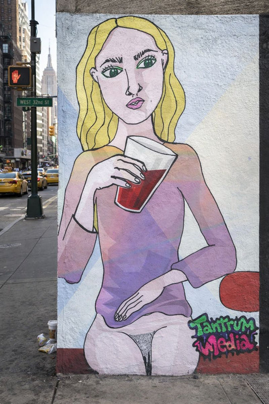 Street mural Koka Cola Girl by Social Tantrum, showing a stylized blonde woman with large green eyes holding a cup on a busy New York City corner.