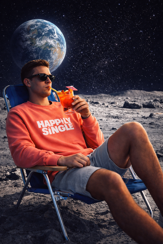 Gen Z man relaxing on the moon in a beach chair, sipping a red cocktail, wearing the Happily Single Unisex Sweatshirt with bold white text, against a cinematic space backdrop with Earth visible in the sky.