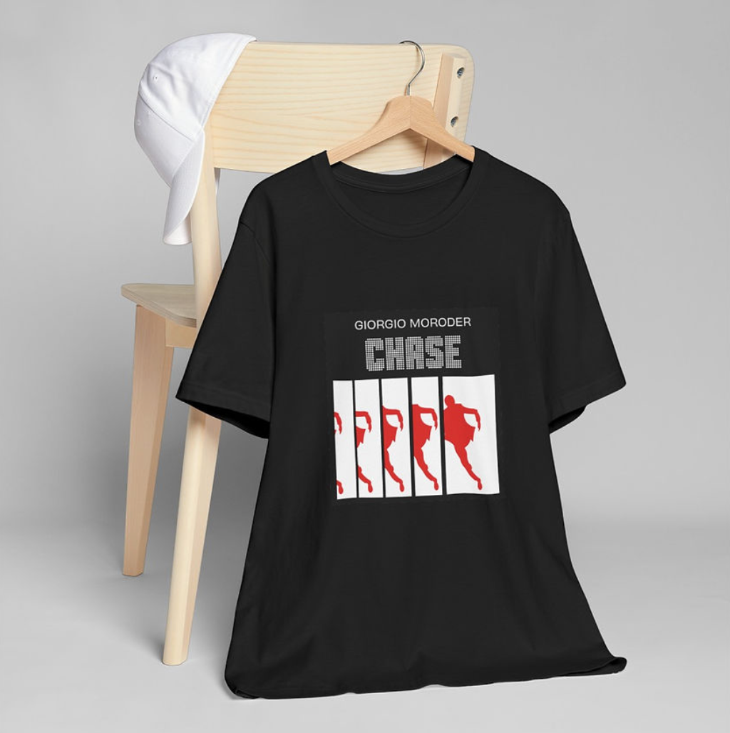 Black Giorgio Moroder "Chase" t-shirt featuring red silhouette artwork, hanging on a wooden chair with a white cap draped over the backrest.