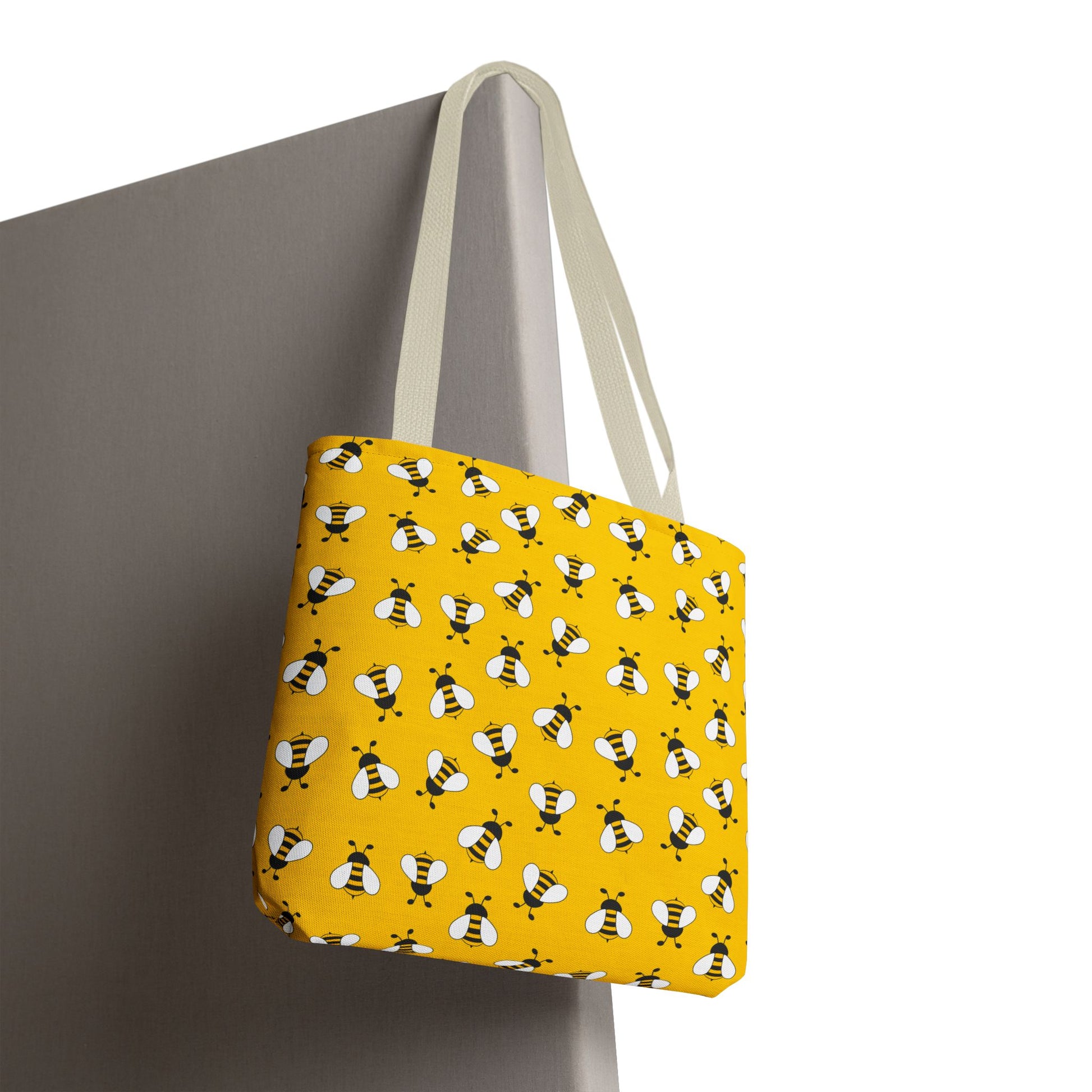 Yellow tote bag with bee pattern hanging on a gray surface