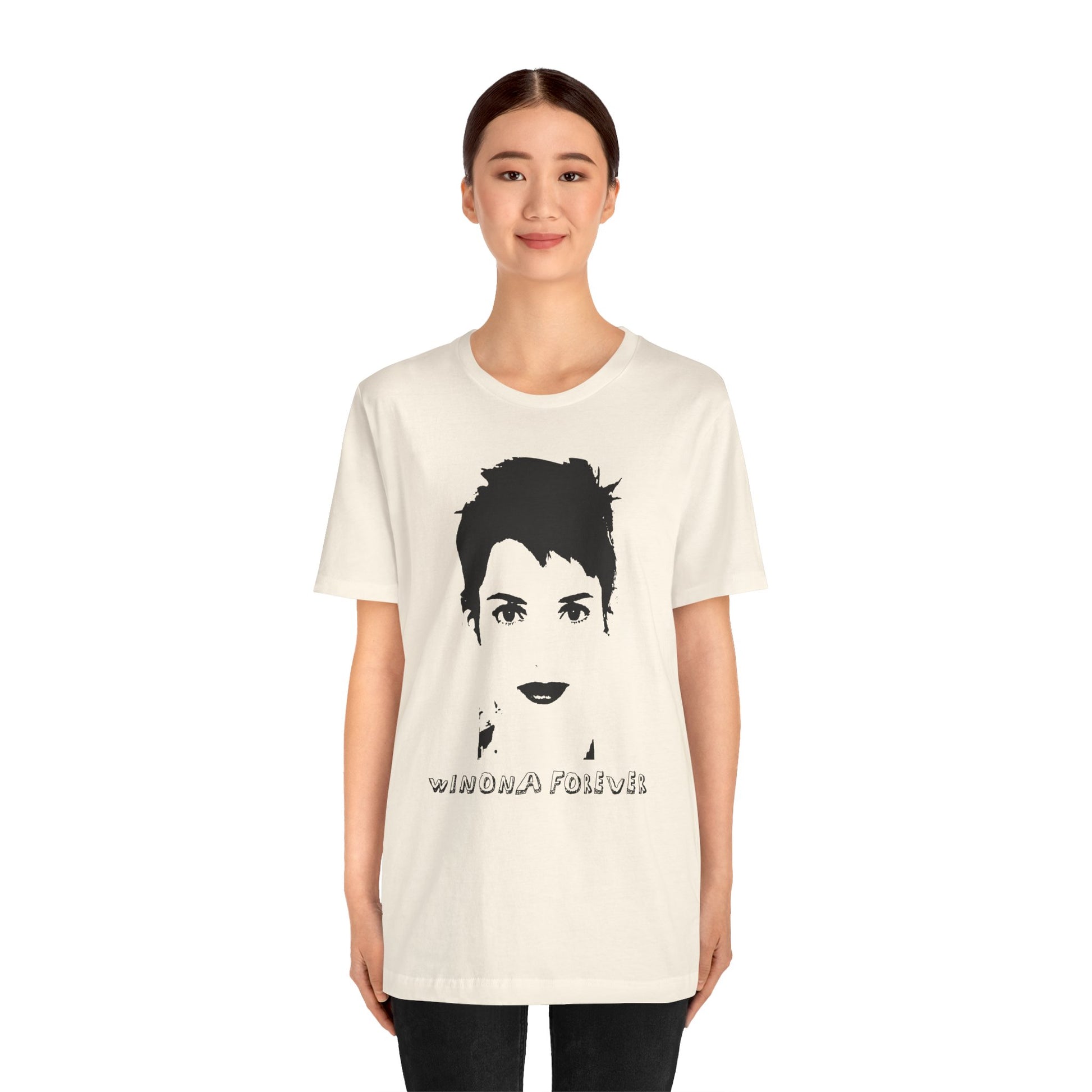 Person wearing a cream Winona Forever T-shirt featuring a minimalist black portrait of Winona Ryder.
