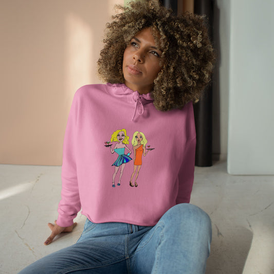 Model wearing the Waitress Crop Unisex Hoodie in pink featuring original waitress artwork, seated casually indoors