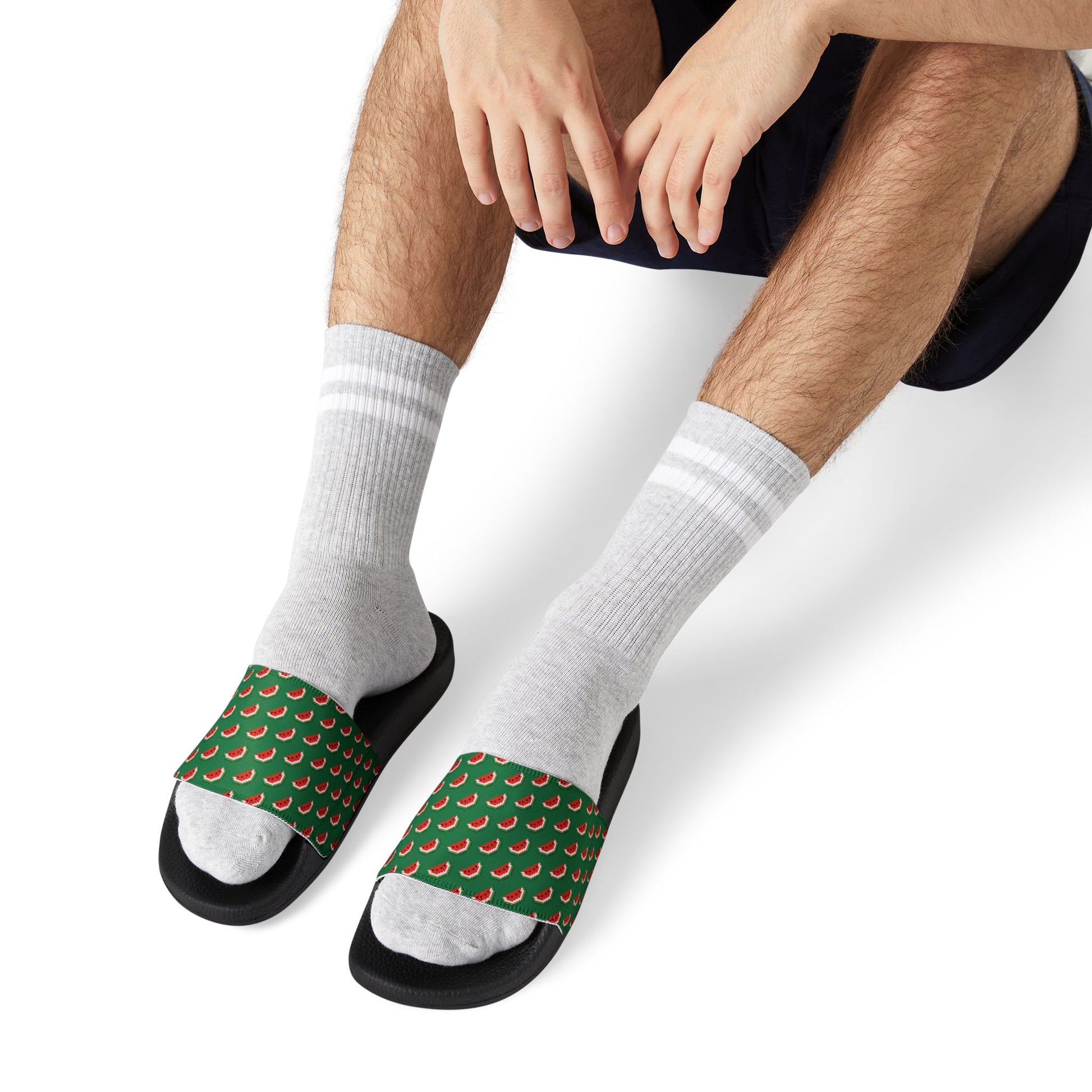 Man seated adjusting Watermelon Green Slide Sandals with black soles and patterned straps over white socks.