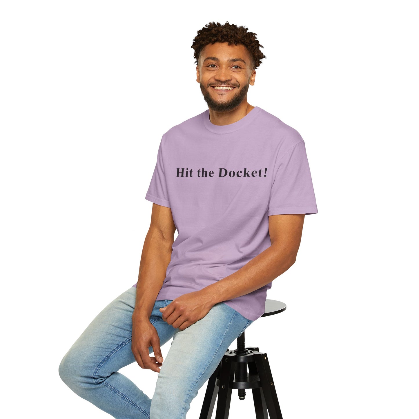 Man wearing a purple t-shirt with 'Hit the Docket!' text, sitting on a stool against a white background