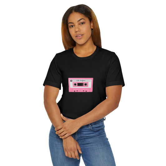 Woman wearing black t-shirt with pink cassette tape graphic, standing casually.