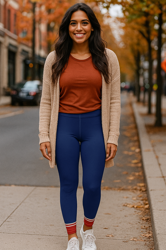 Woman wearing blue leggings with red and white striped cuffs, paired with a rust shirt and beige cardigan, walking on a city street lined with fall trees.