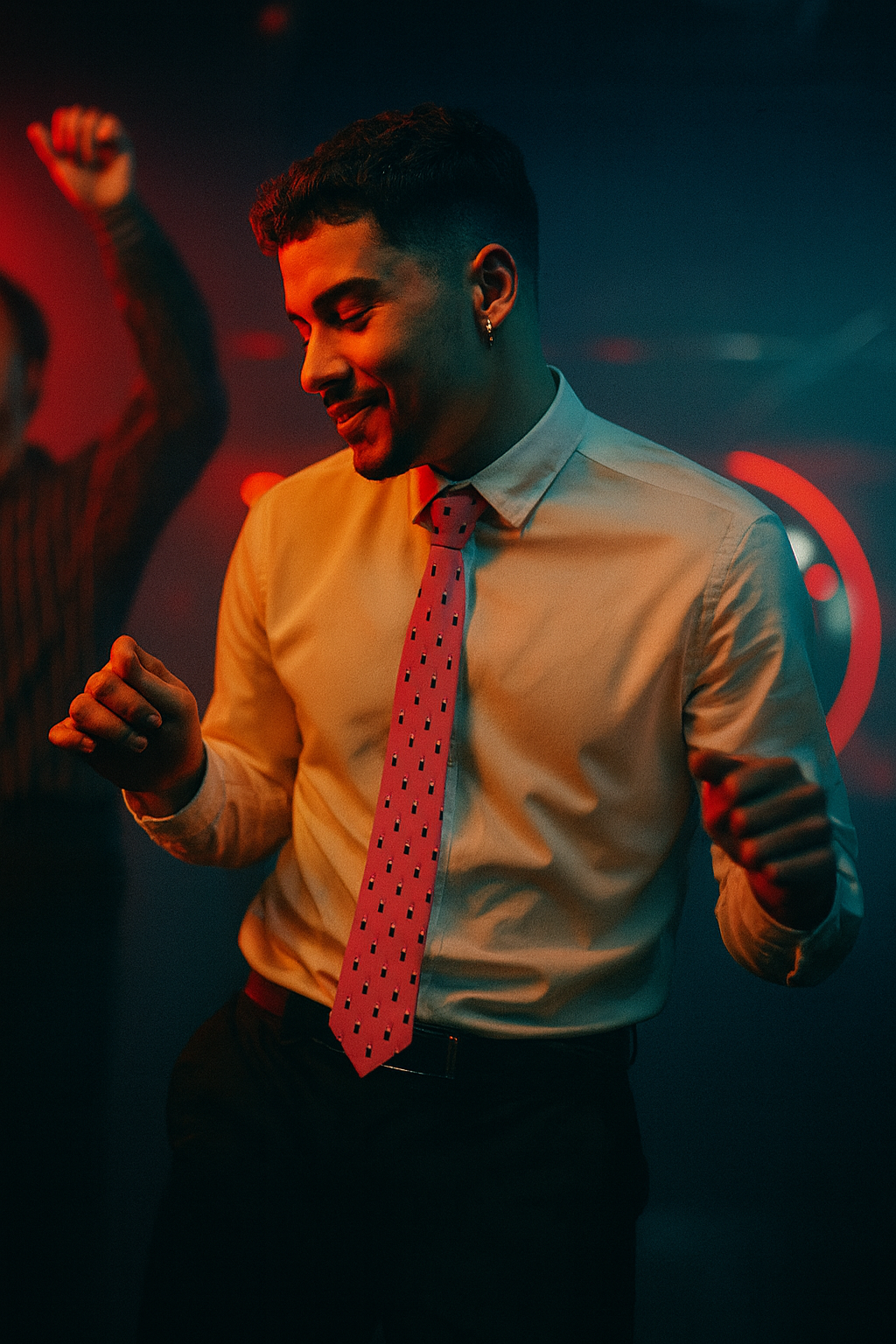 Man wearing a pink lipstick patterned necktie while dancing under colorful lights, representing bold nightlife and expressive fashion.