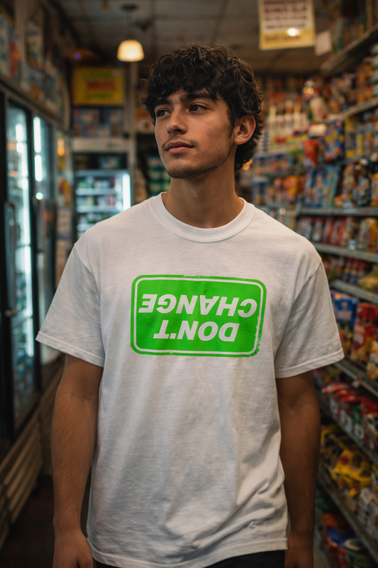 Man wearing a white Don’t Change T-Shirt with a bright green upside down graphic, standing in a convenience store aisle with a relaxed streetwear vibe.