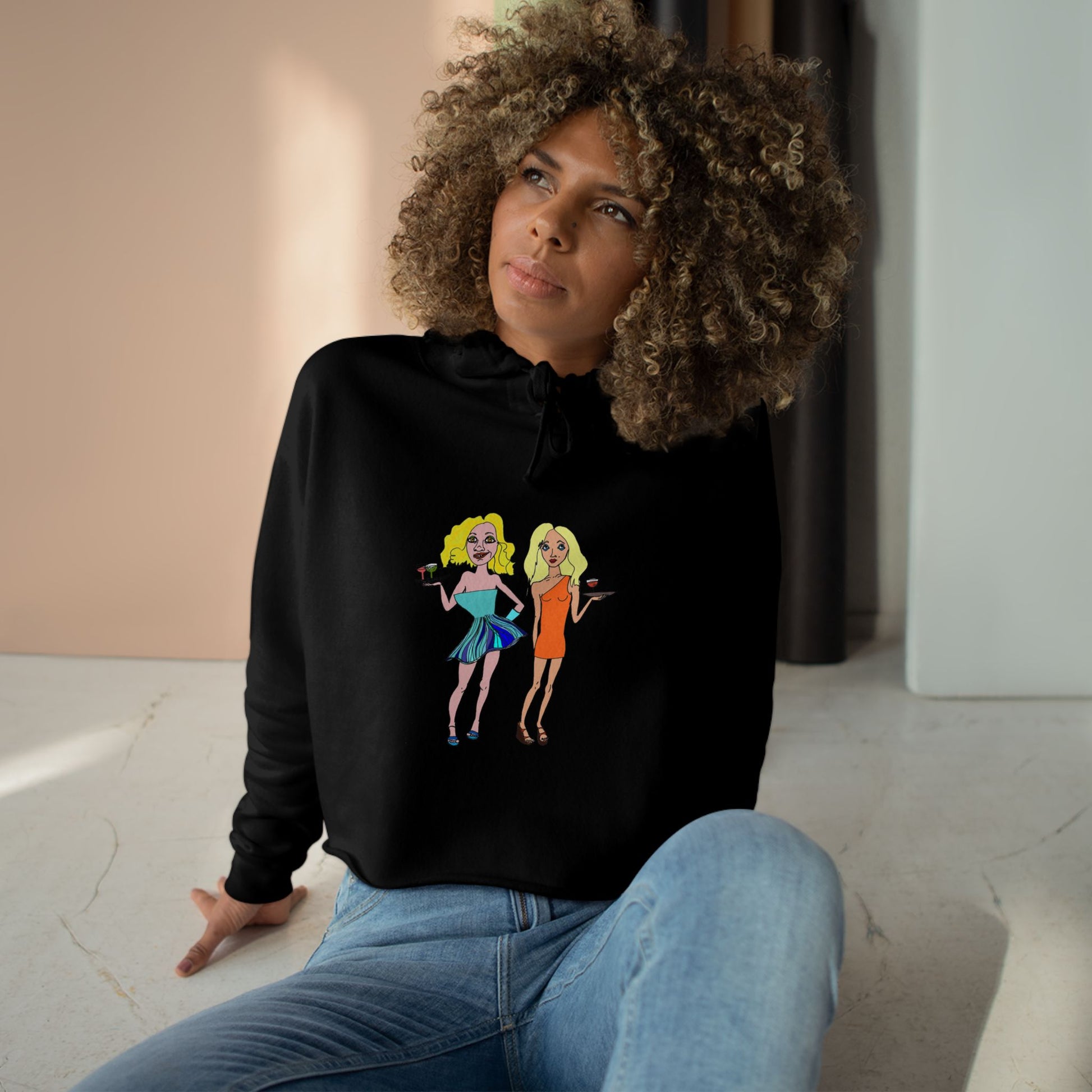 Model wearing the black Waitress Crop Unisex Hoodie with original waitress artwork, seated indoors