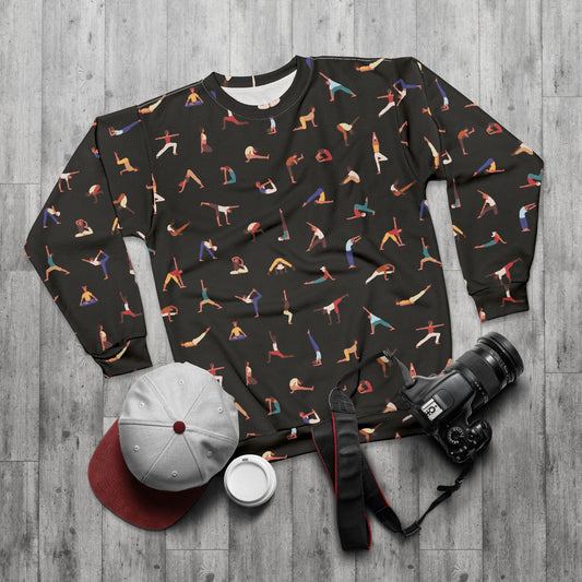 Black sweatshirt with colorful yoga pose pattern on a wooden surface with camera, cap, and cup.