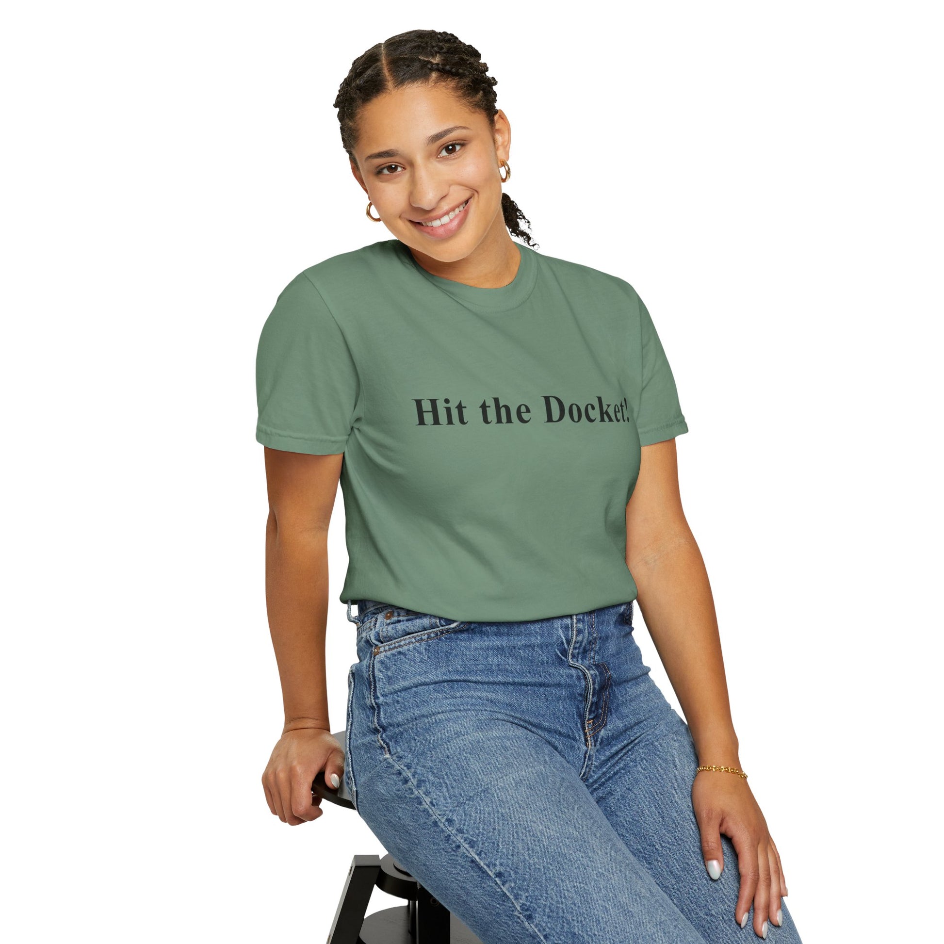 Person wearing a green t-shirt with 'Hit the Dockets' text and blue jeans, sitting on a stool against a white background.