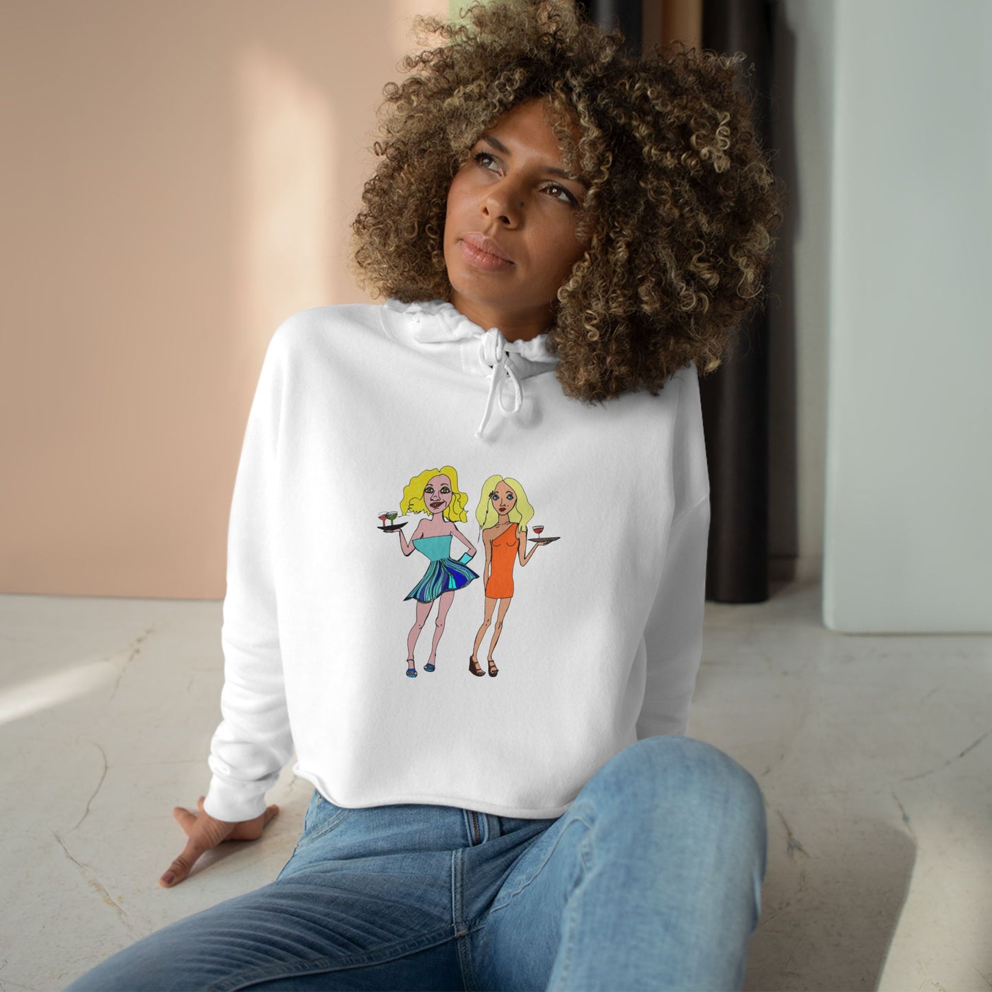 Model wearing the white Waitress Crop Unisex Hoodie with original waitress artwork, seated on the floor
