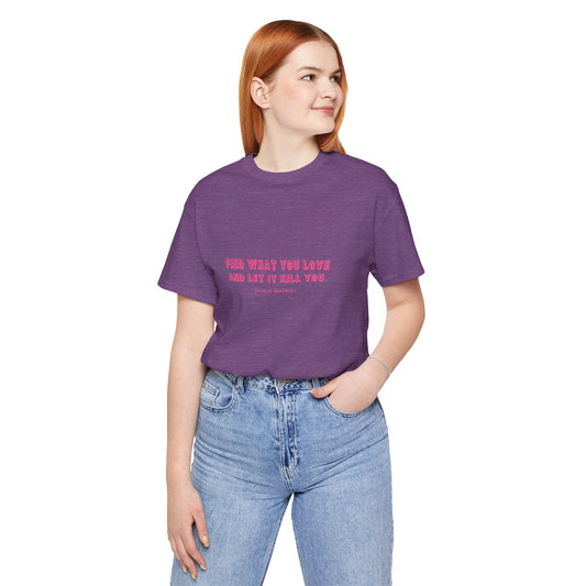 Woman wearing a purple Bukowski quote t-shirt with tucked-in jeans.