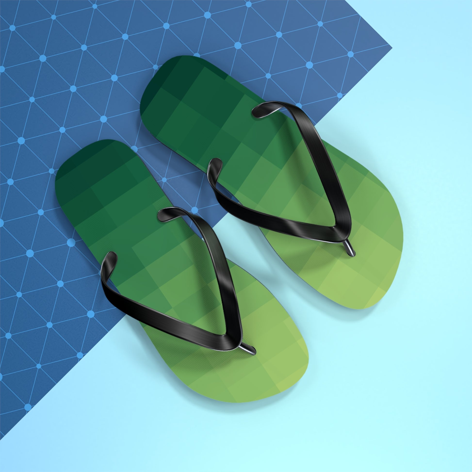 Green pixel-art inspired flip flops with black straps photographed on a bright geometric blue background