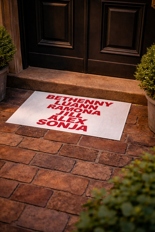 OG NY Housewives outdoor rug placed on brick entryway, white mat with bold red cast names graphic, patio decor lifestyle shot