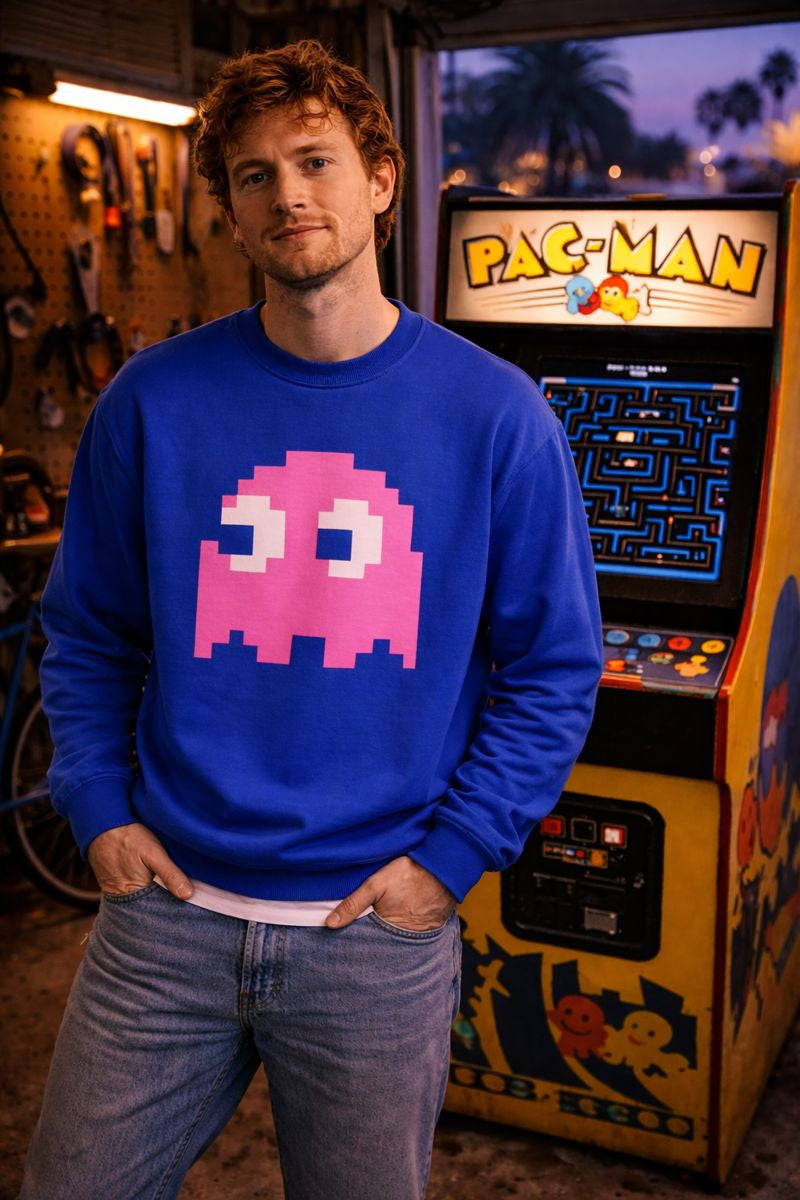 Person wearing a blue sweatshirt with a pink ghost design in front of a Pac-Man arcade machine.