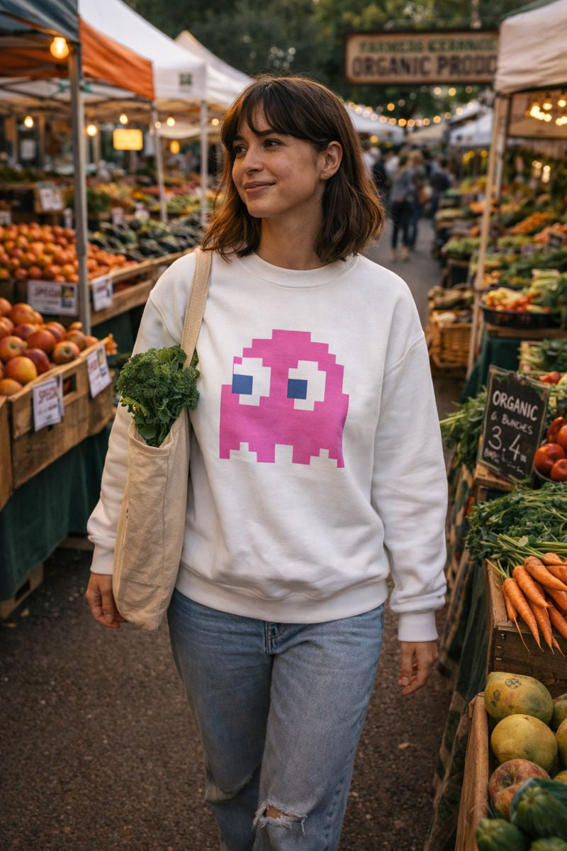 Woman wearing a white sweatshirt with a pink and blue graphic at an outdoor farmers market.