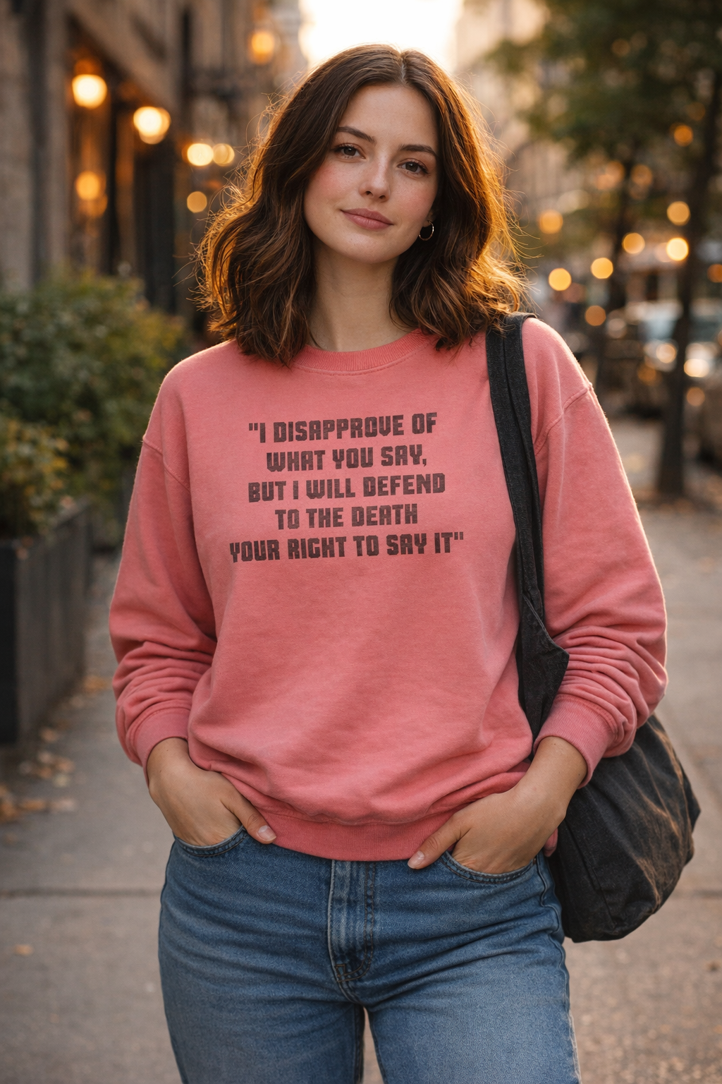 Millennial woman wearing a coral Freedom of Speech sweatshirt on a city sidewalk at golden hour.